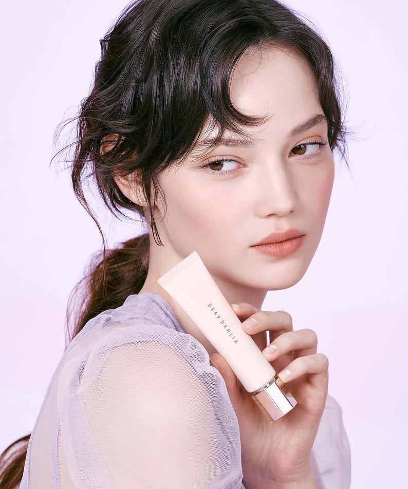 Model holding DEAR DAHLIA Prime Layer Blurring Primer, enhancing soft-focus effect for flawless skin, perfect for beauty enthusiasts.