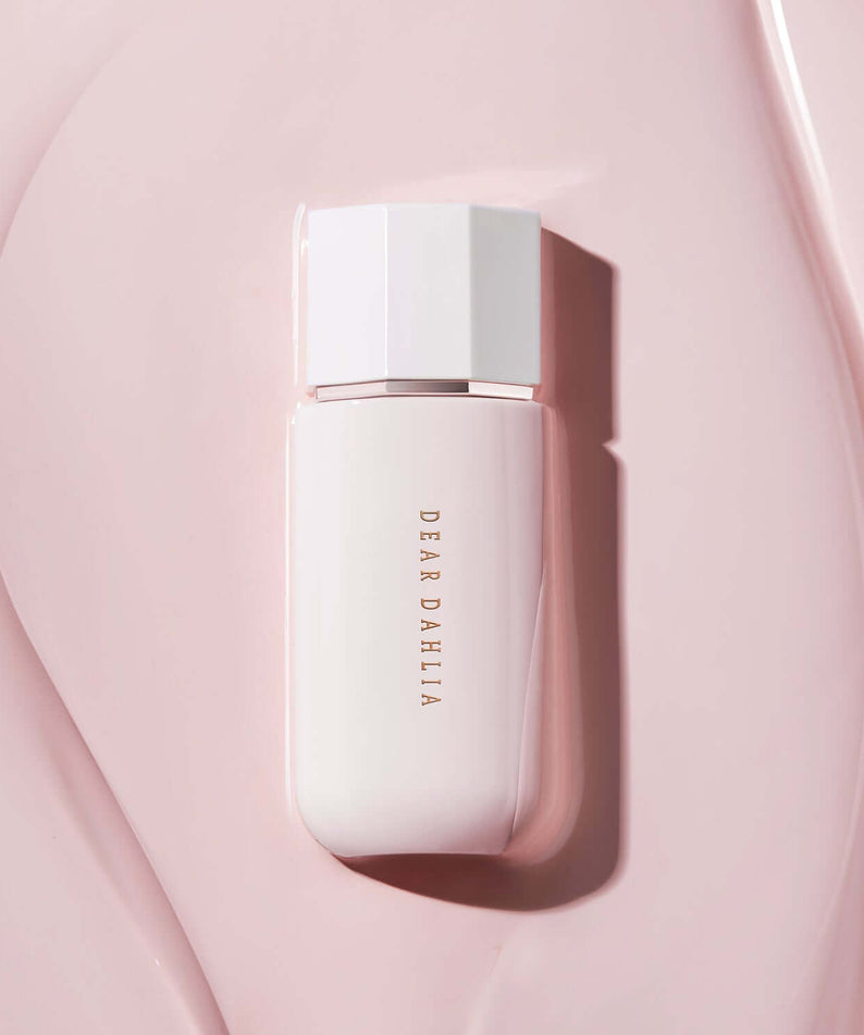DEAR DAHLIA Prime Layer Glow Primer bottle on pink surface