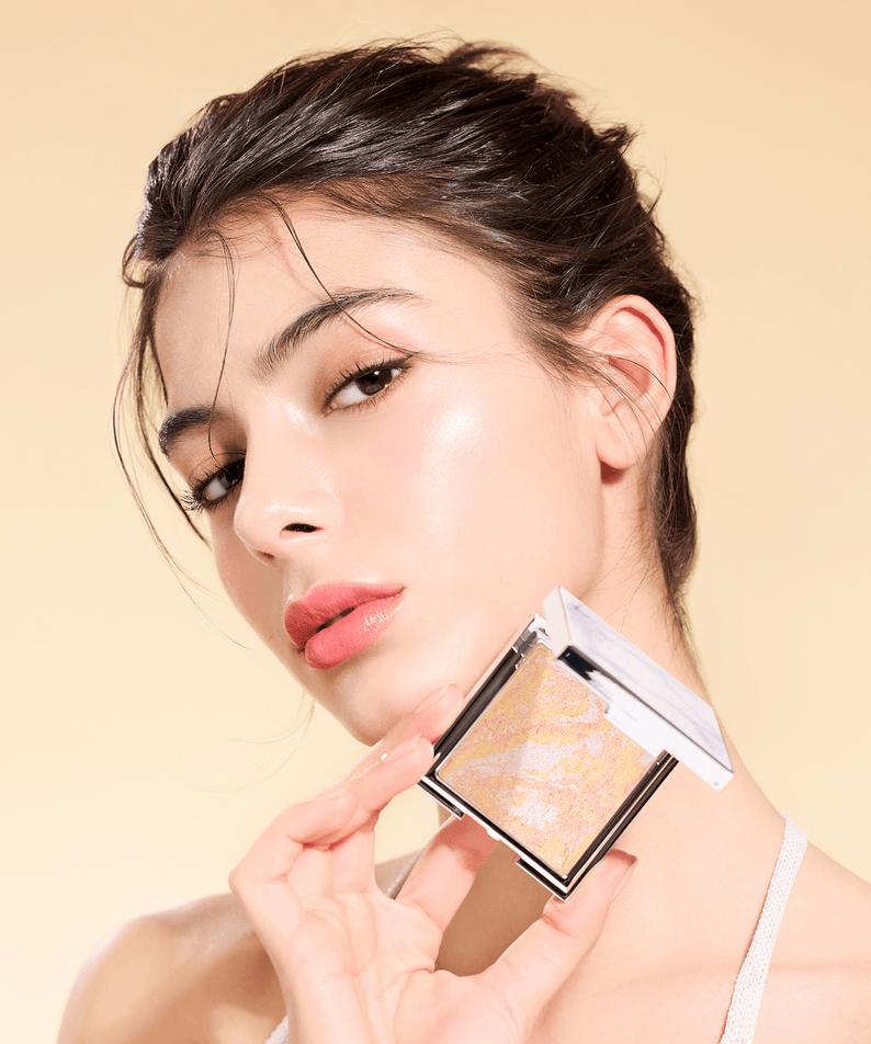 Woman holding DEAR DAHLIA Skin Luminous Highlighter against a soft beige background.