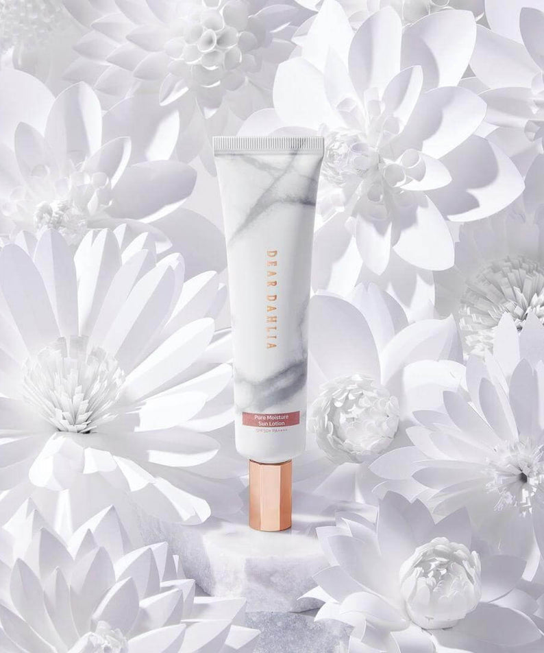 DEAR DAHLIA Skin Paradise Pure Moisture Sun Lotion surrounded by white flowers in a luxurious display