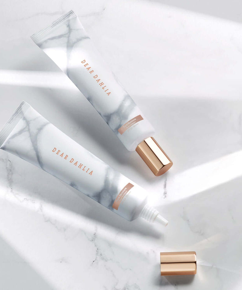 DEAR DAHLIA Skin Paradise Pure Moisture Sun Lotion on marble surface with rose gold caps.