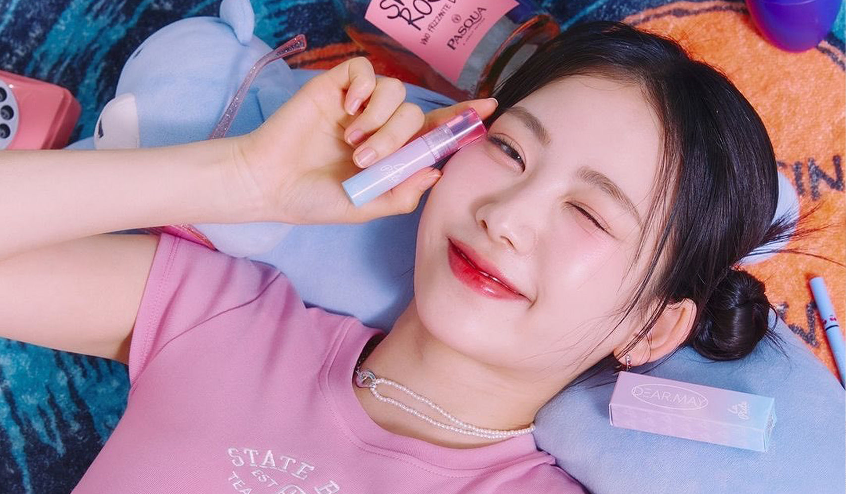 Smiling woman holding lip gloss, lying on colorful blanket, playful and relaxed beauty scene