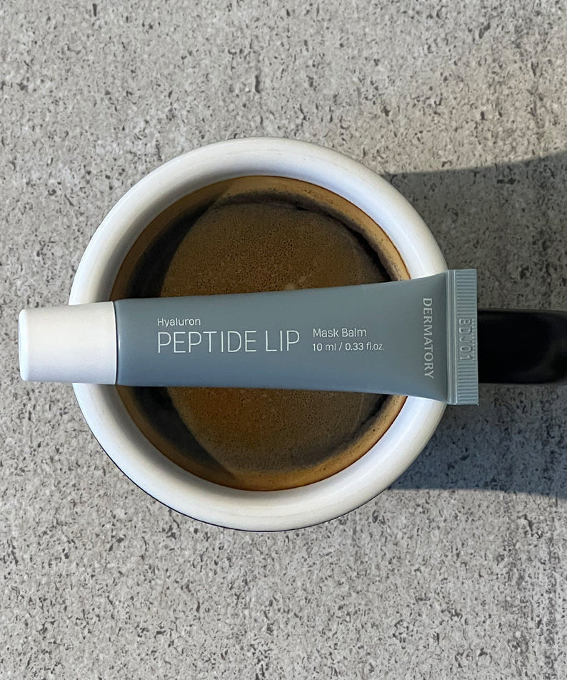 DERMATORY Hyaluronic Peptide Lip Keyring balm tube resting on a coffee cup top view
