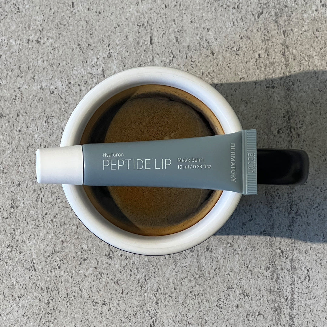 DERMATORY Hyaluronic Peptide Lip Keyring balm tube resting on a coffee cup top view