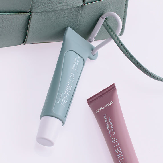 DERMATORY Hyaluronic Peptide Lip Keyring with attached mint tube, displayed alongside the pink version, styled on a handbag.