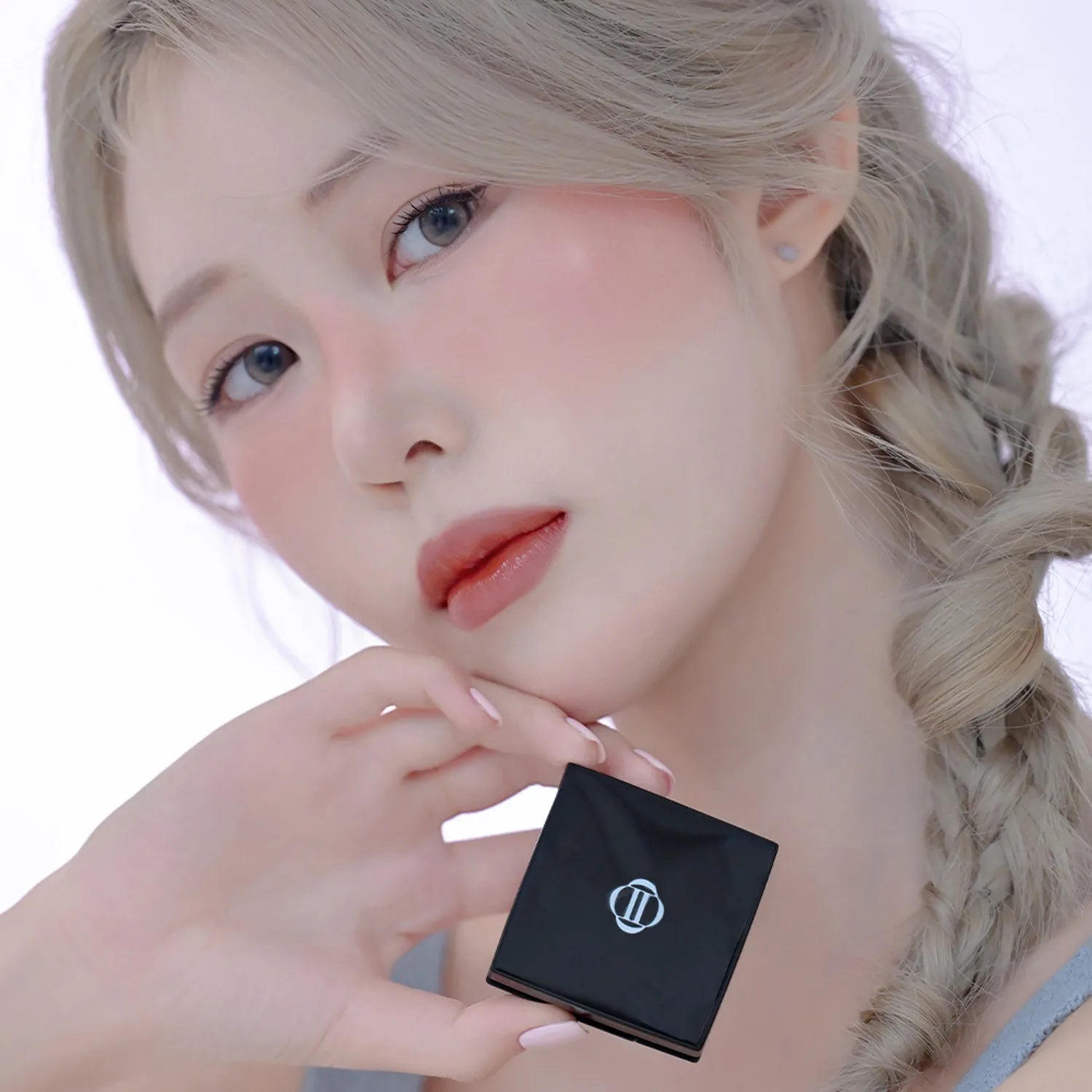 Model holding DINTO Be My Wendy Blusher with natural makeup and braided hair.
