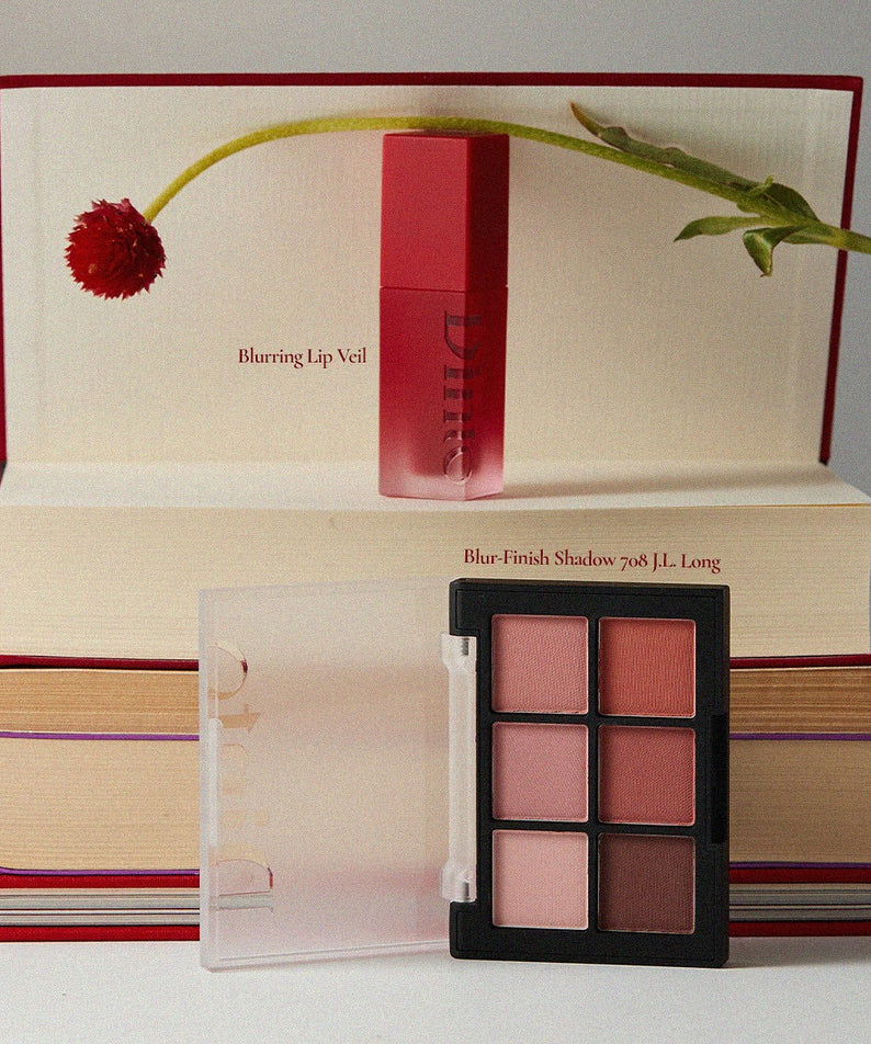 DINTO Blurring Lip Veil with palette on books, showcasing beauty products.