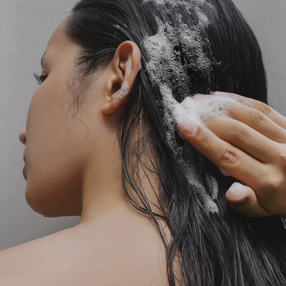 Person using DONGGUBAT Correct Shampoo Bar For Dry Skin on wet hair, creating a lather, highlighting its benefits for dry scalp care.