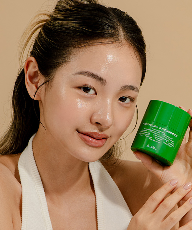 Person holding DR ALTHEA Pure Grinding Cleansing Balm showcasing product packaging with a soft beige background.