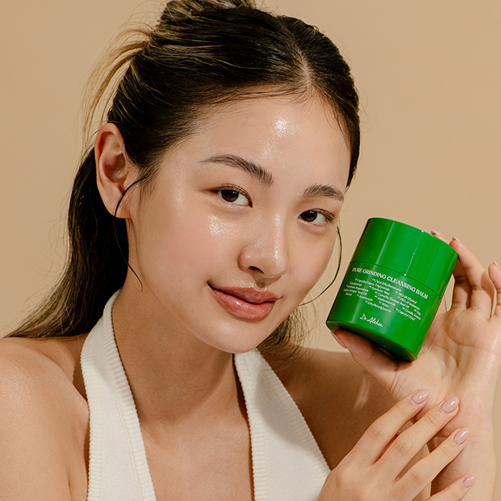 Person holding DR ALTHEA Pure Grinding Cleansing Balm showcasing product packaging with a soft beige background.