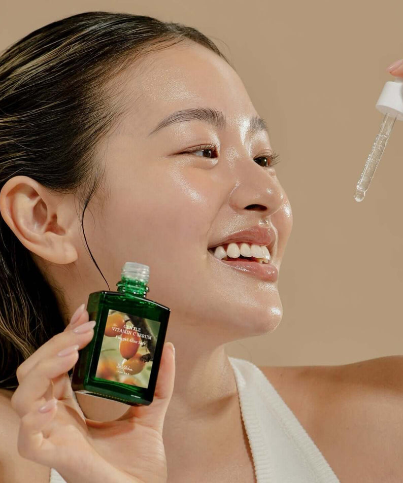 Smiling woman applying DR.ALTHEA Gentle Vitamin Serum 30ml with dropper, showcasing skincare routine.