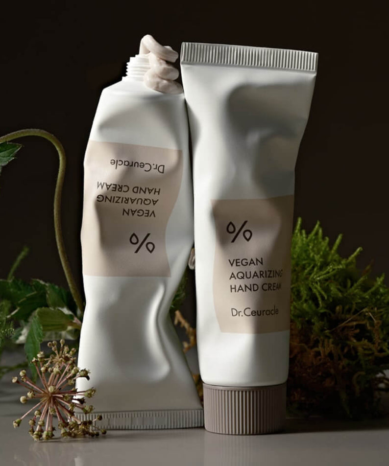 DR.CEURACLE Aqua Rising Hand cream 50ml packaging against a natural background with green plants and flowers.