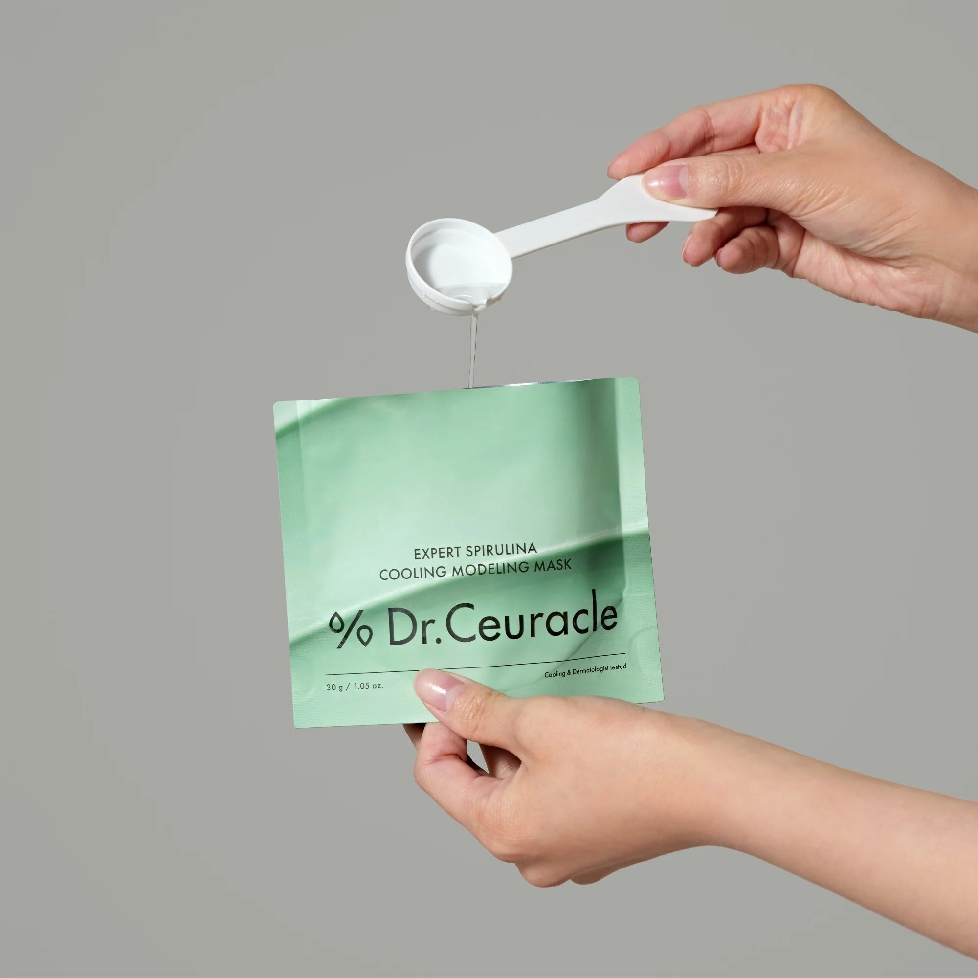 Hands holding DR.CEURACLE Expert Spirulina Cooling Modeling Mask 30g with spoon.