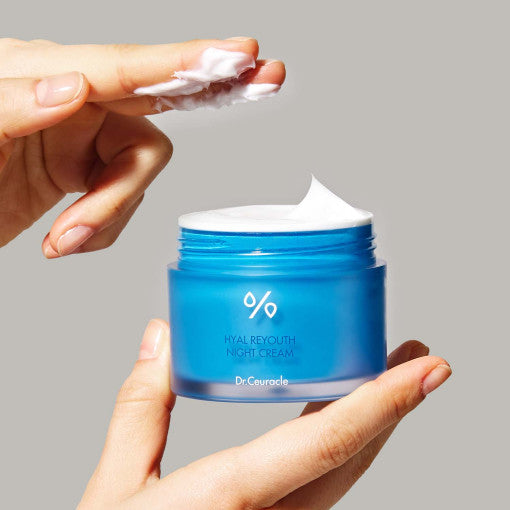 Hands holding DR.CEURACLE Hyal Reyouth Night Cream 60g jar with cream texture, showcasing product texture.