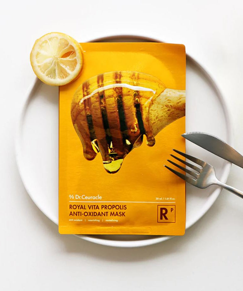 DR.CEURACLE Royal Vita Propolis Glow Mask (10EA) displayed on a white plate with a lemon slice and cutlery.