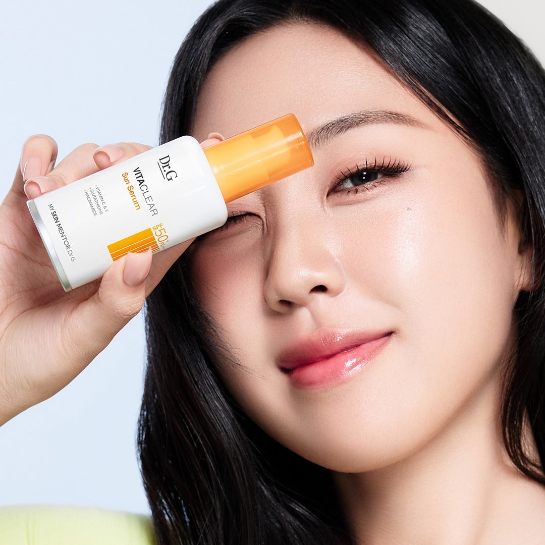 Woman holding DR.G Vita Clear Sun Serum 50ml next to her face showing skincare product application.