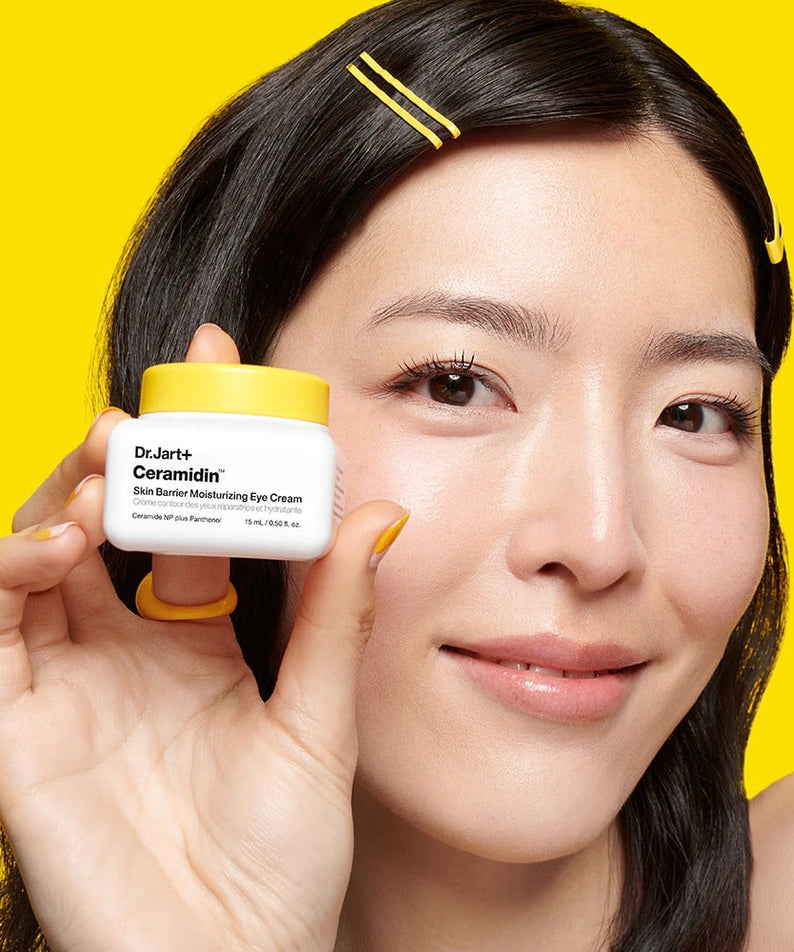 DR.JART+ Ceramidin Skin Barrier Moisturizing Eye Cream 15ml bottle held by model against yellow background.