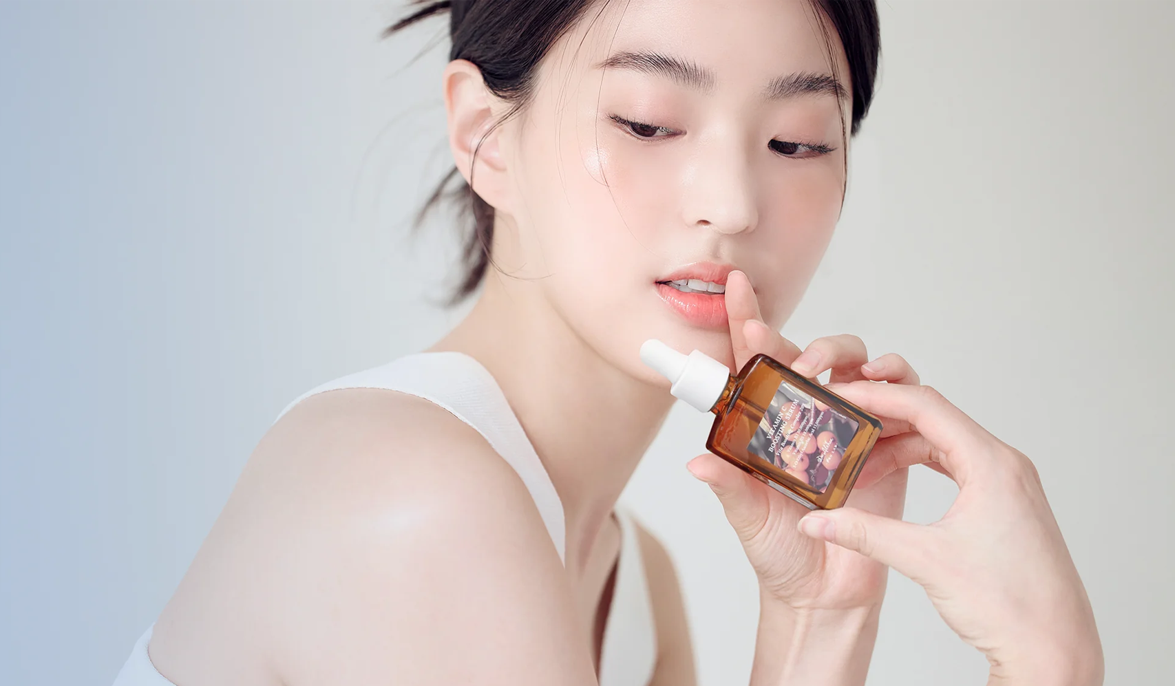 Person holding a dropper bottle of skincare serum near their face
