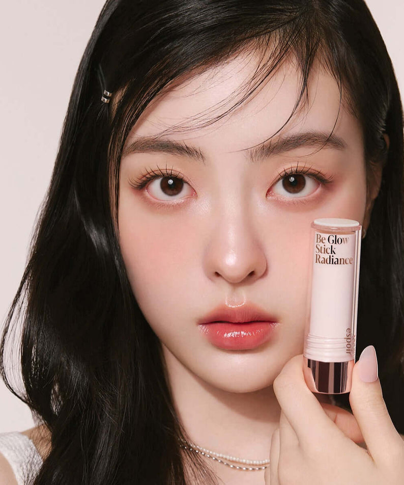 Woman holding ESPOIR BE GLOW STICK RADIANCE near face.