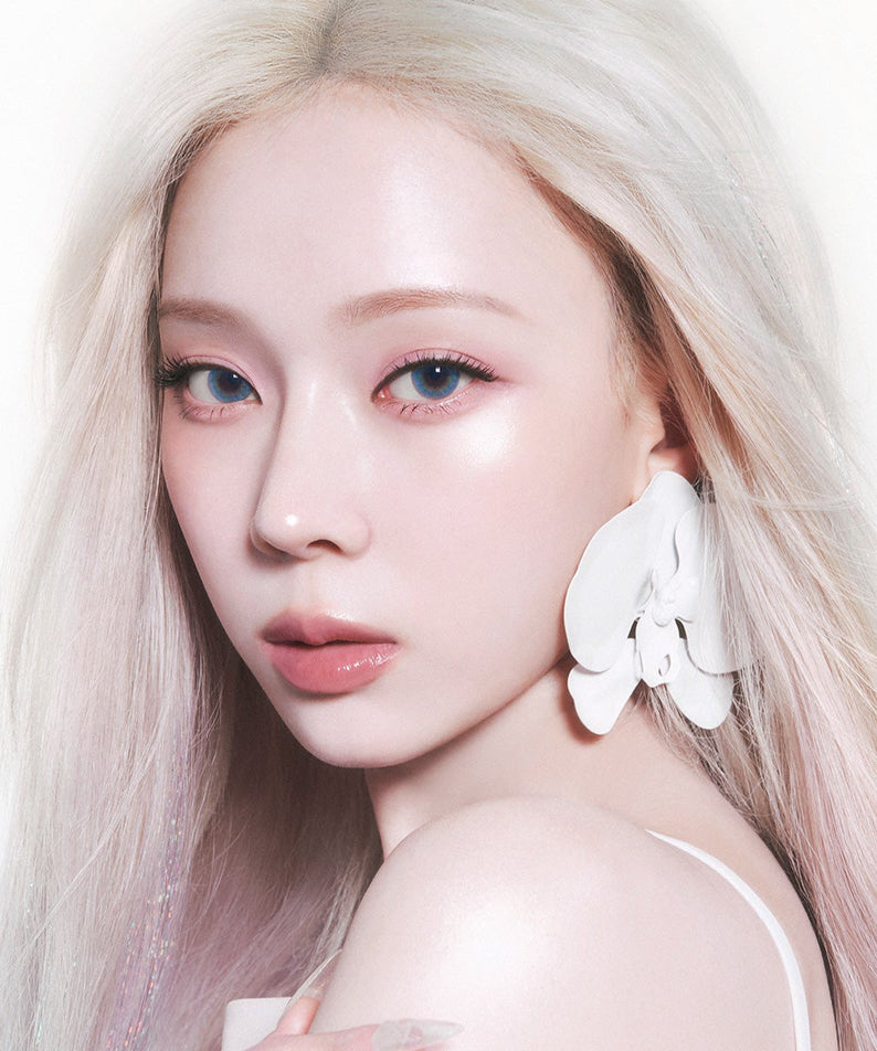 Portrait of a woman with platinum blonde hair and large white earrings, showcasing a glowing complexion.