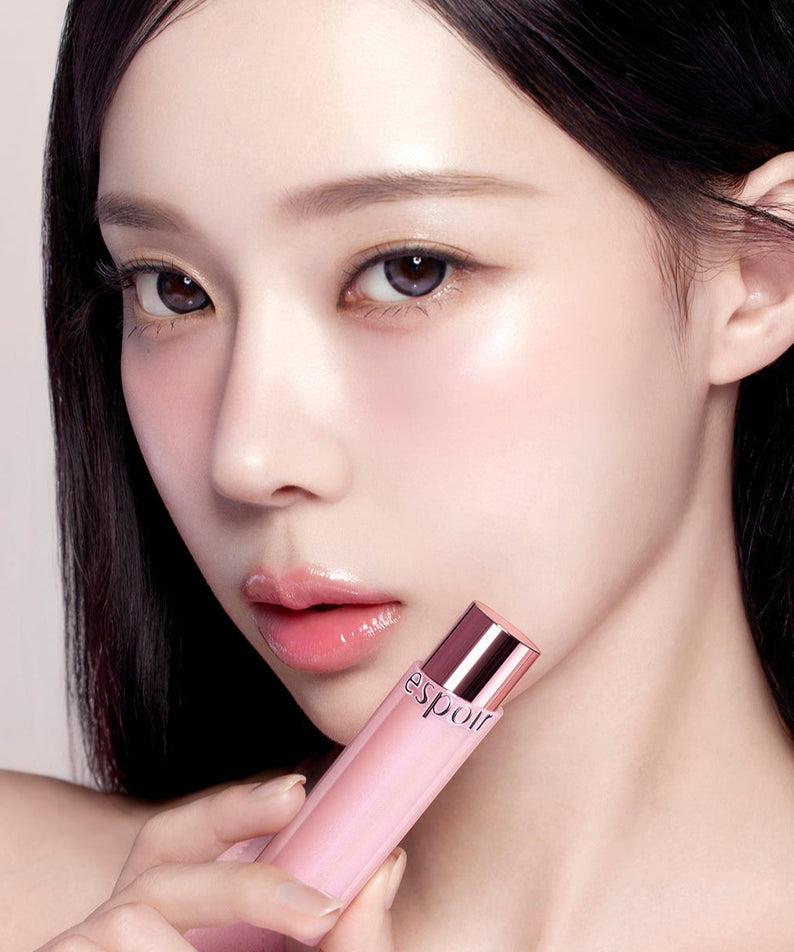 Close-up of woman holding ESPOIR Bare Glow Lip Balm, showcasing the product's packaging and its luminous finish on lips.