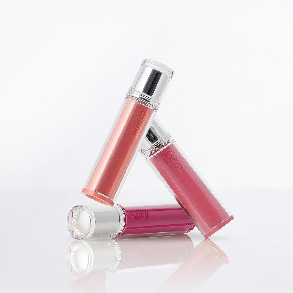 ESPOIR Couture Lip Tint Glaze in three shades, showcasing elegant packaging on a reflective surface.