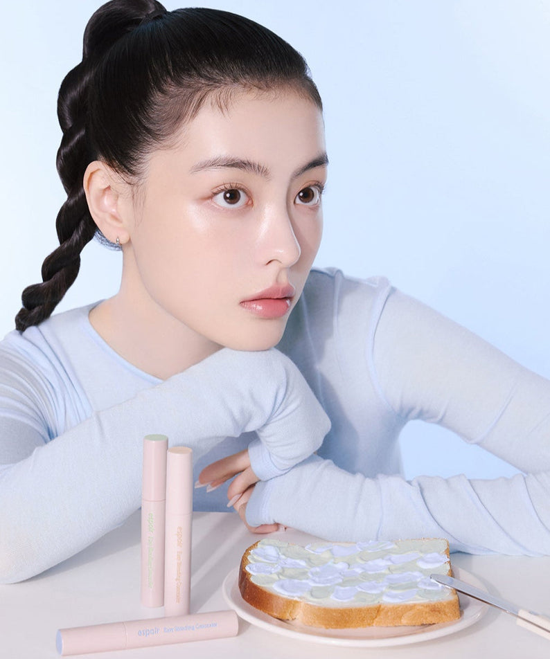 Model posing with ESPOIR EASY BLENDING CONCEALER next to toast on a plate, showcasing skincare and makeup product.
