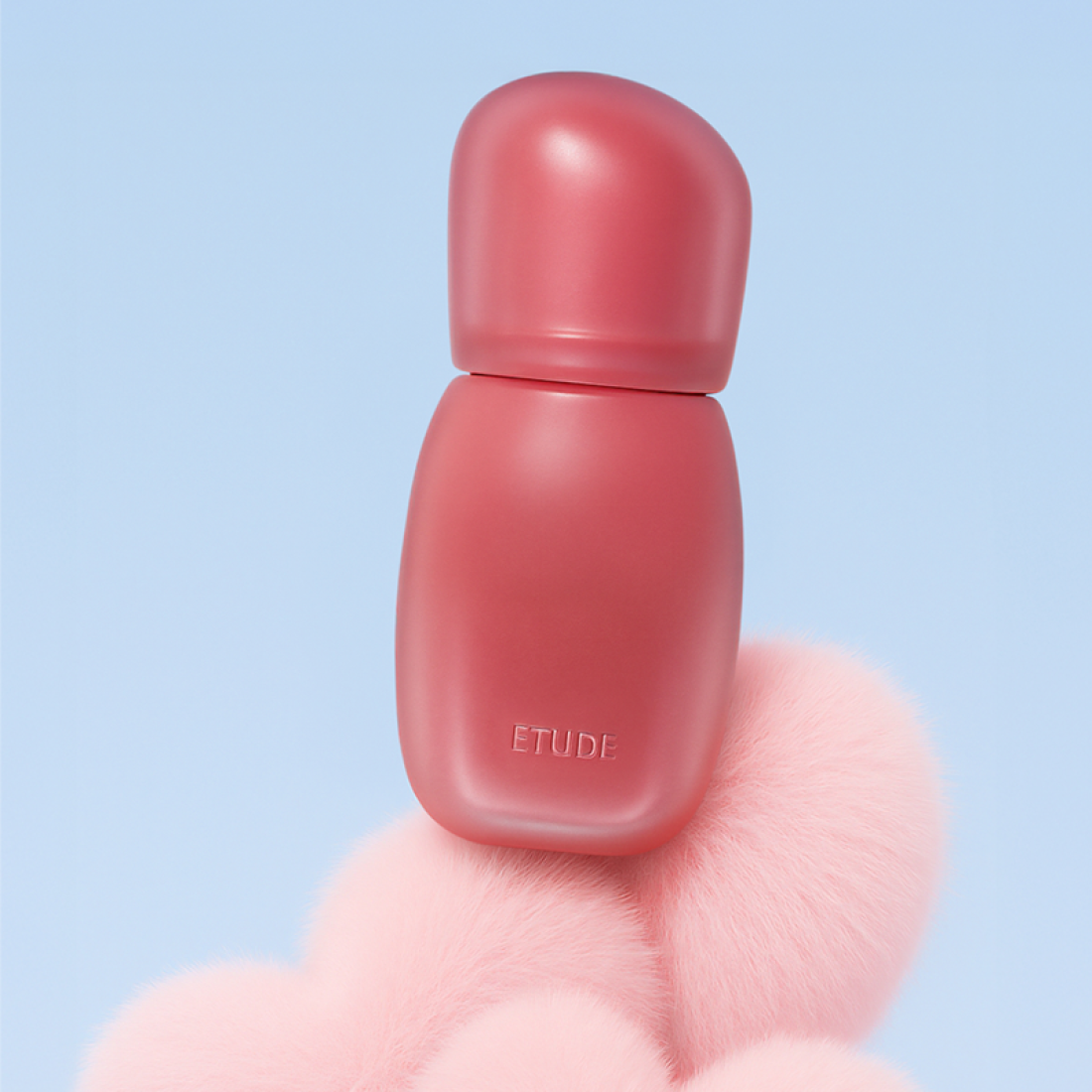 ETUDE Cozy Fixing Tint 4g in pink bottle, standing on fluffy pink surface against blue background.
