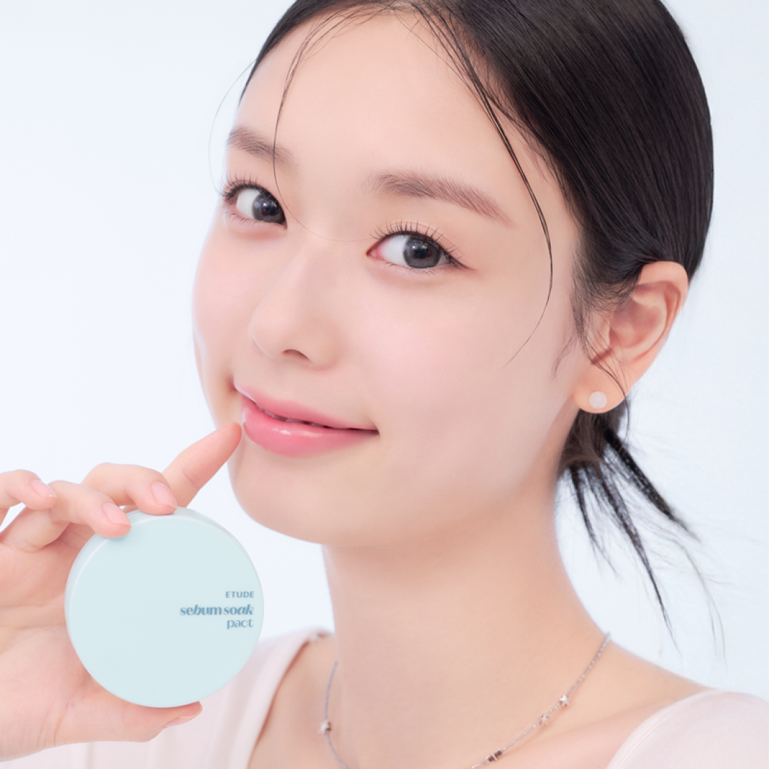 Close-up of a person holding ETUDE Fiji Ssok Pact 9.5g next to their face, showcasing its packaging and potential usage.