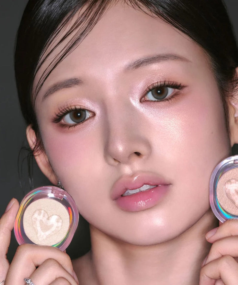 Woman holding ETUDE Shooting Beam Highlighter 3g with heart design, showing shimmering glow on cheekbones.