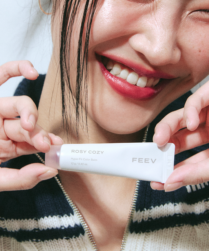 Smiling individual holding FEEV Hyper-Fit Color Balm in a close-up shot.