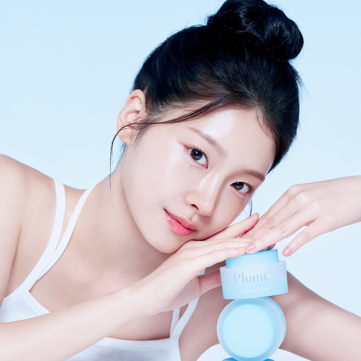 Model holding FORENCOS Plum C Mild Cleansing Balm 50ml, showcasing skincare product on a light blue background.