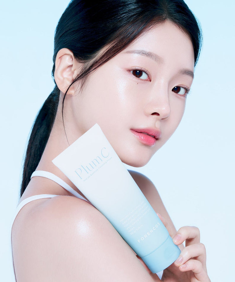 Woman holding FORENCOS Plum C Mild Mild Acidic Cleansing Foam 150g against blue background, showcasing skincare product.
