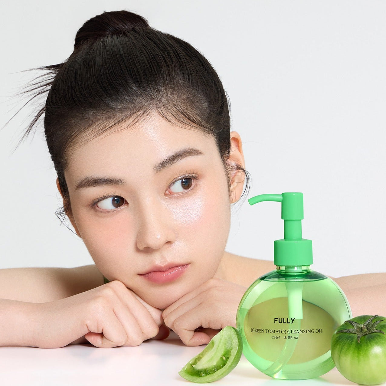 Woman with FULLY Green Tomato Cleansing Oil 250ml bottle and green tomato slice in a skincare setting