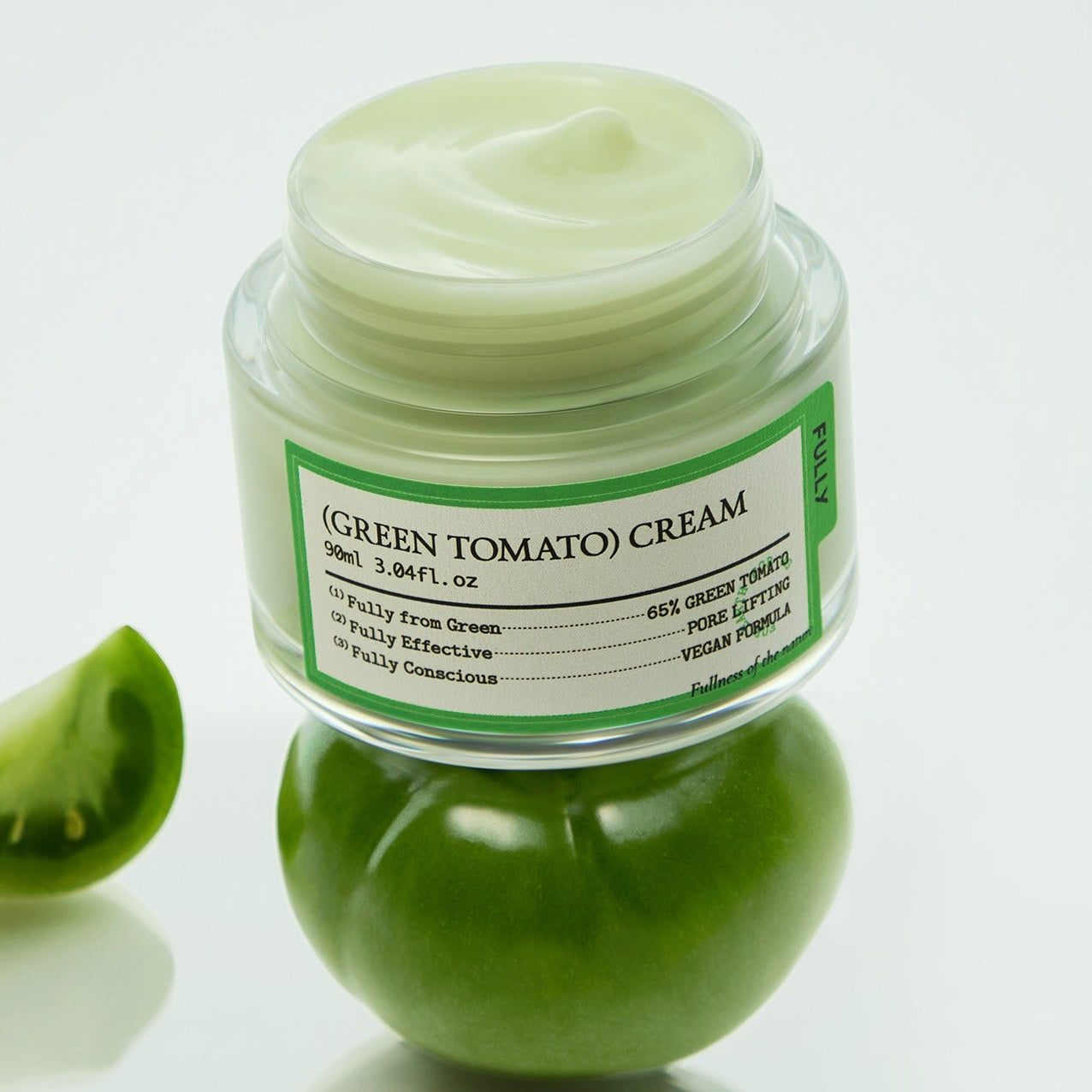 Image of FULLY Green Tomato Cream 90ml jar resting on fresh green tomato, highlighting eco-friendly skincare product.