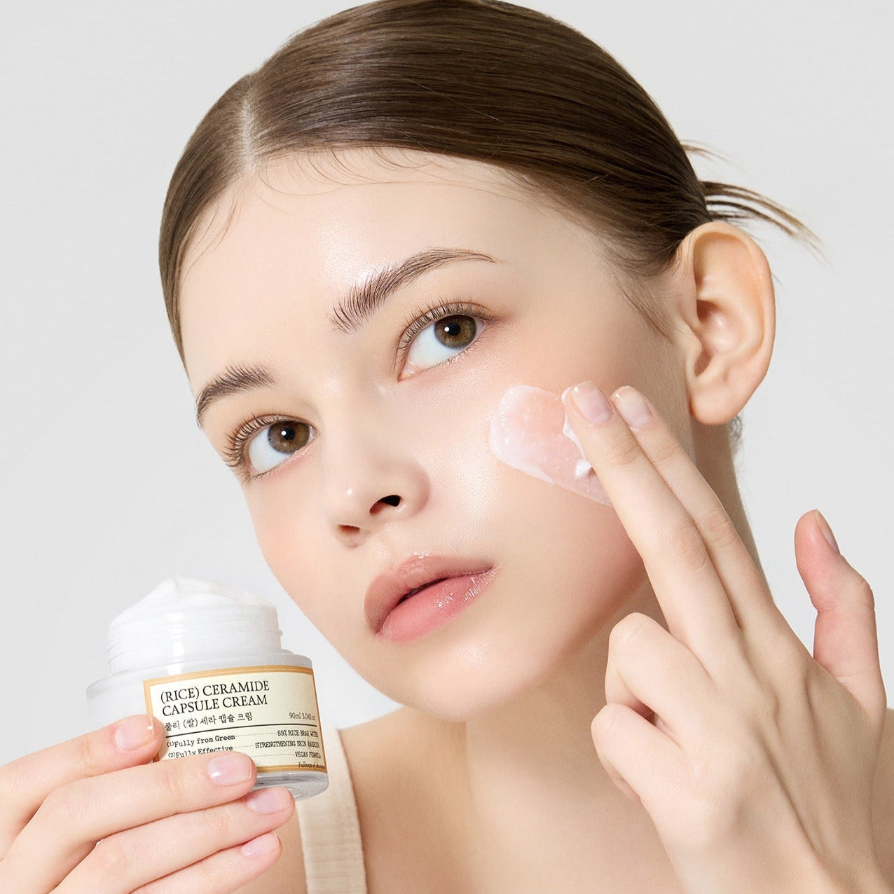 Woman applying FULLY Rice Sera Capsule Cream 90ml skincare product to her face for moisture and care.