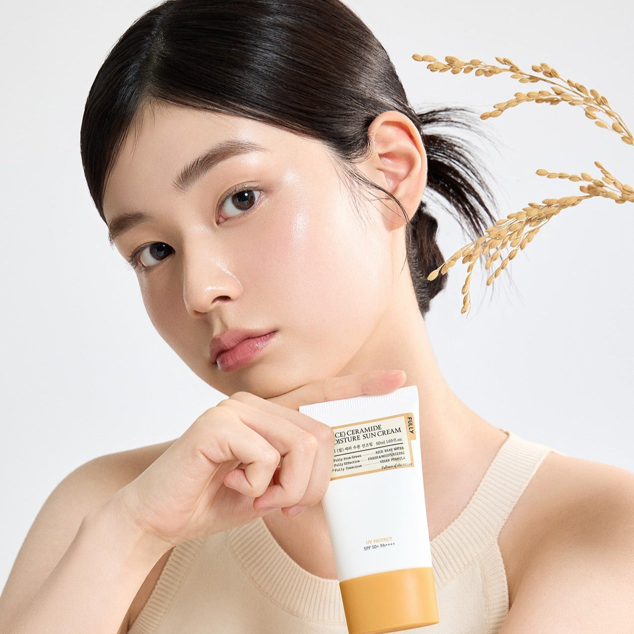 Woman holding FULLY Rice Sera Moisture Sunscreen 50ml with rice plant in the background