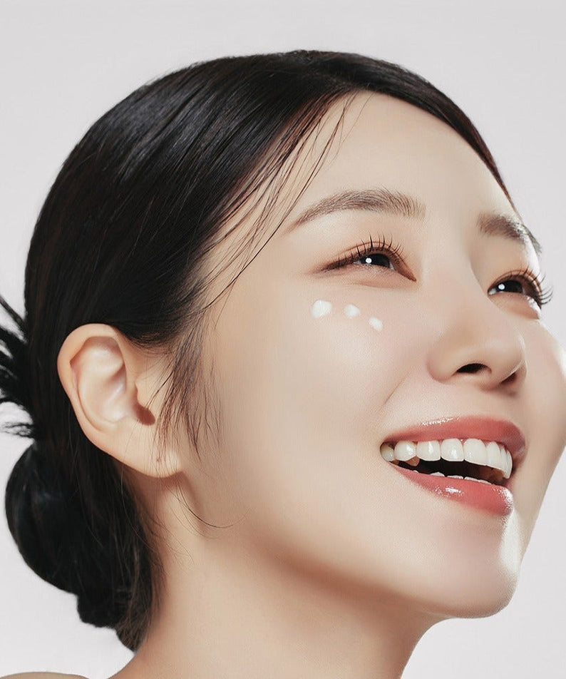 Smiling woman applying skincare, showcasing the brightening effect of GENABELLE PDRN Enriched Recovery Balm 50ml on radiant skin.