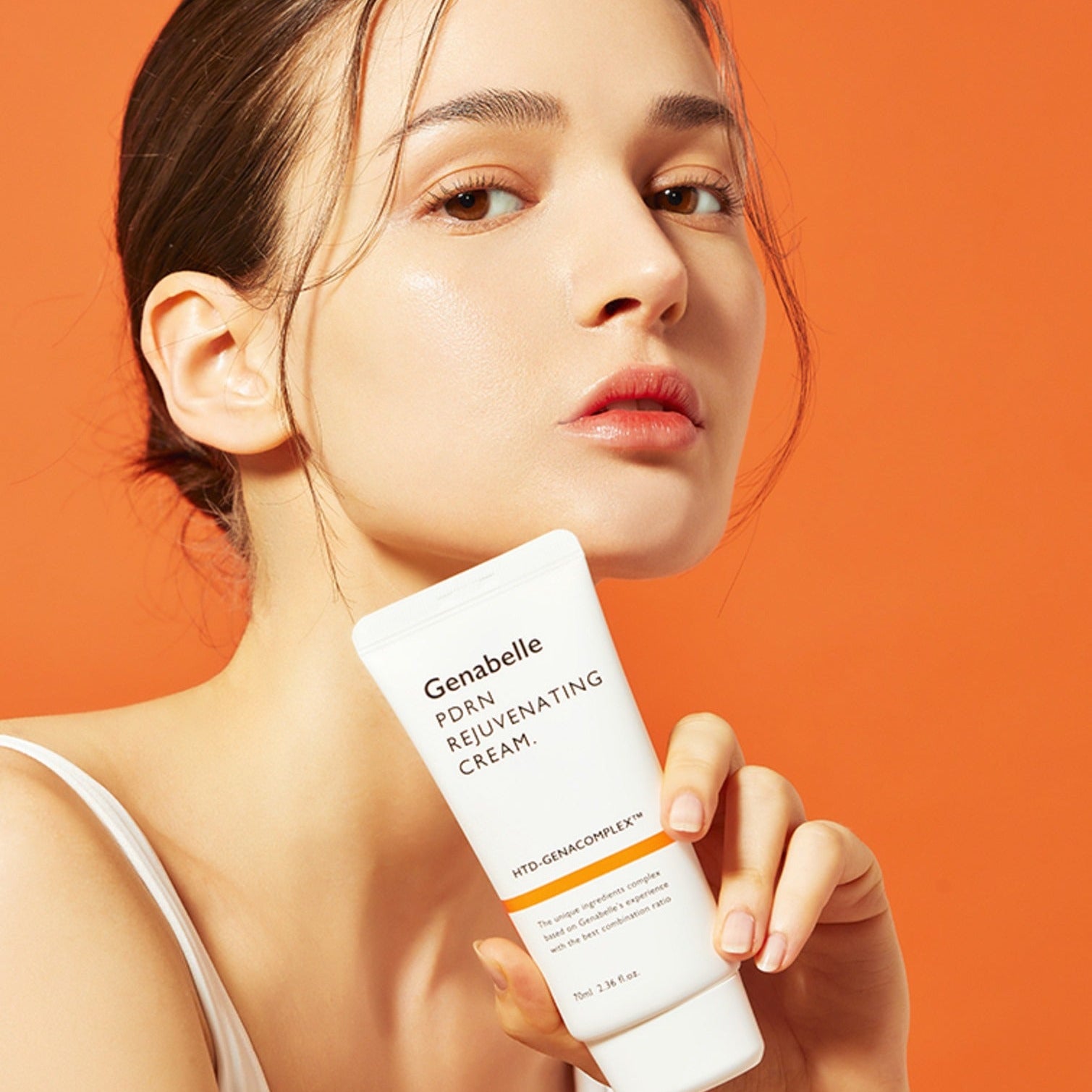 Woman holding GENABELLE PDRN Rejuvenating Cream 70ml against orange background.