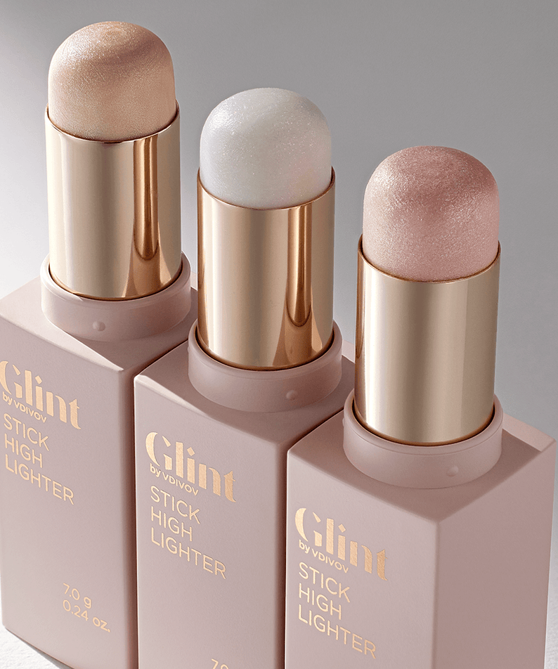 Three shades of GLINT Stick Highlighter in metallic tubes on a glossy surface