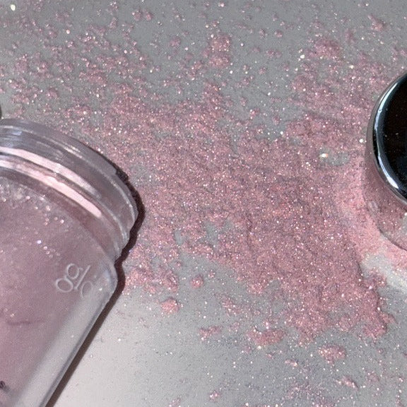GLOW Seasoning Highlighter pink sparkle powder spilled on a shiny surface