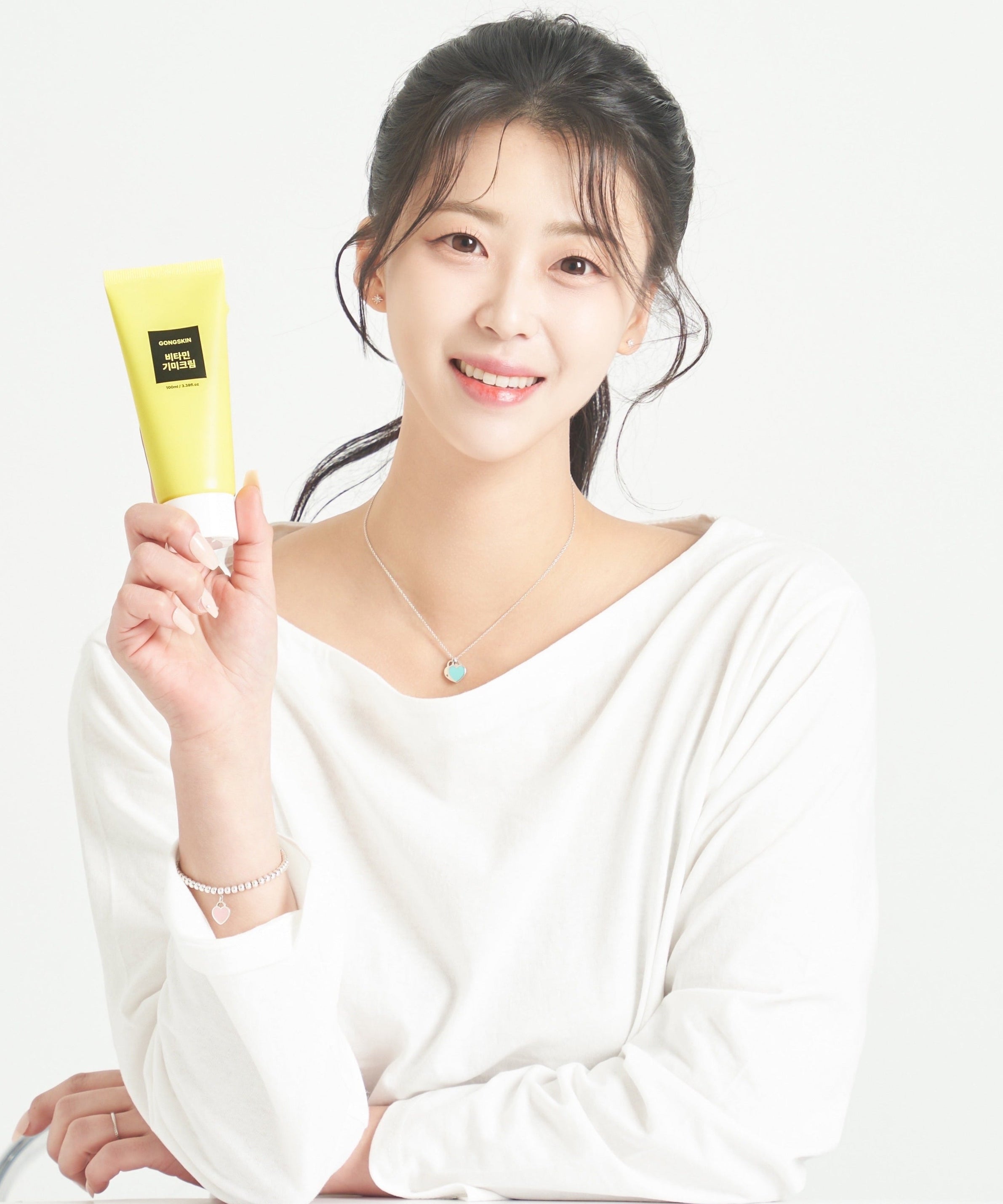 Person holding skincare product in yellow packaging, shown in a light setting.