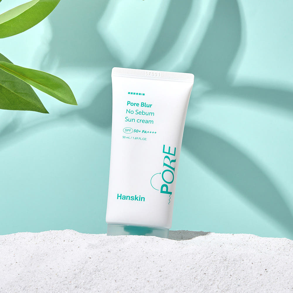 HANSKIN Pore Blur No-Sebum Sunscreen SPF50+ PA++++ 50ml product image on a sandy beach with green leaves.