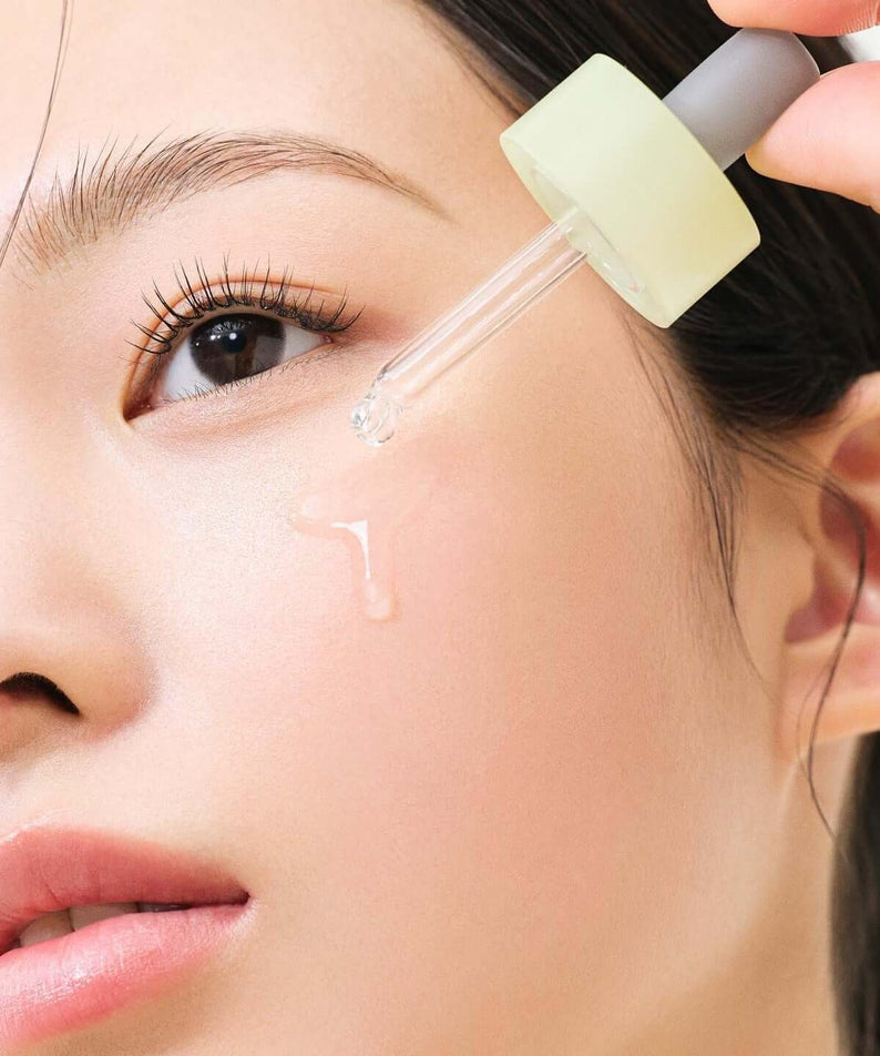 Close-up of woman applying HANYUL Bodunhaengip Pore Fir Serum on face with dropper for skincare.