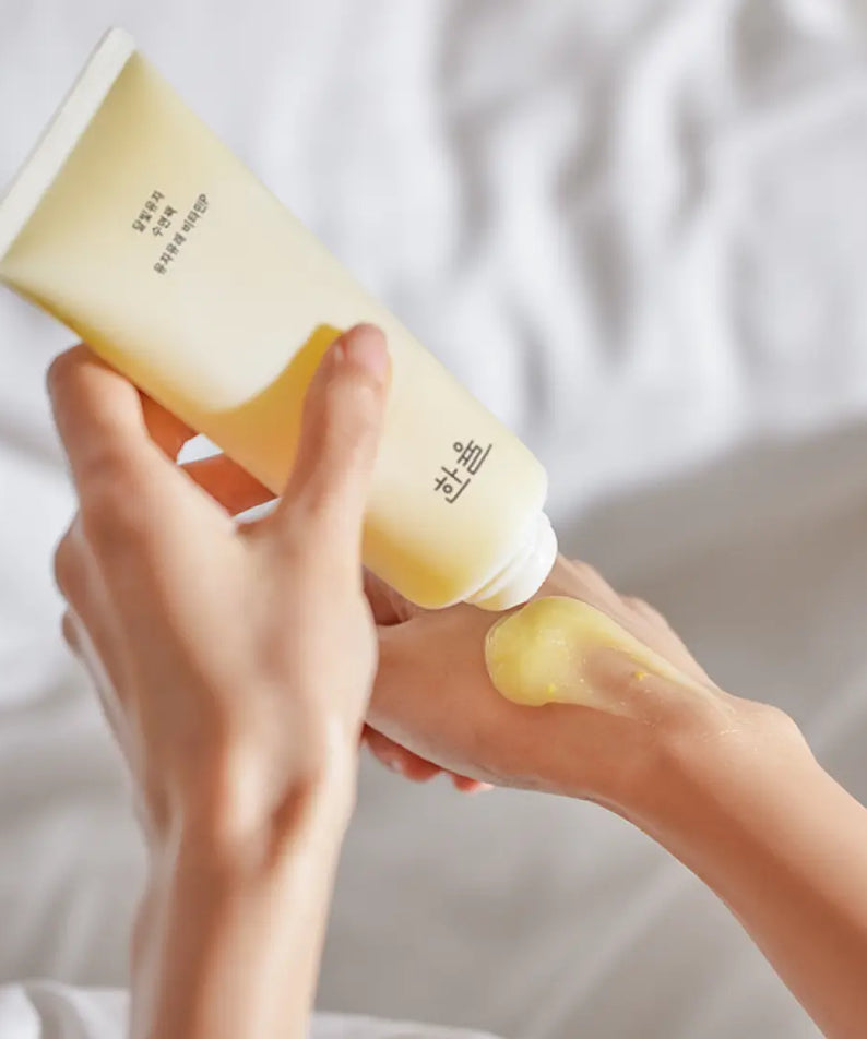 Person applying HANYUL Moonlight Yuja Sleeping Pack 100ml on hand, showcasing texture and packaging.