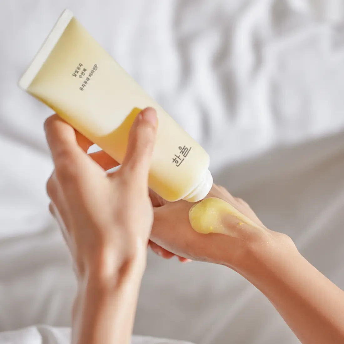 Person applying HANYUL Moonlight Yuja Sleeping Pack 100ml on hand, showcasing texture and packaging.