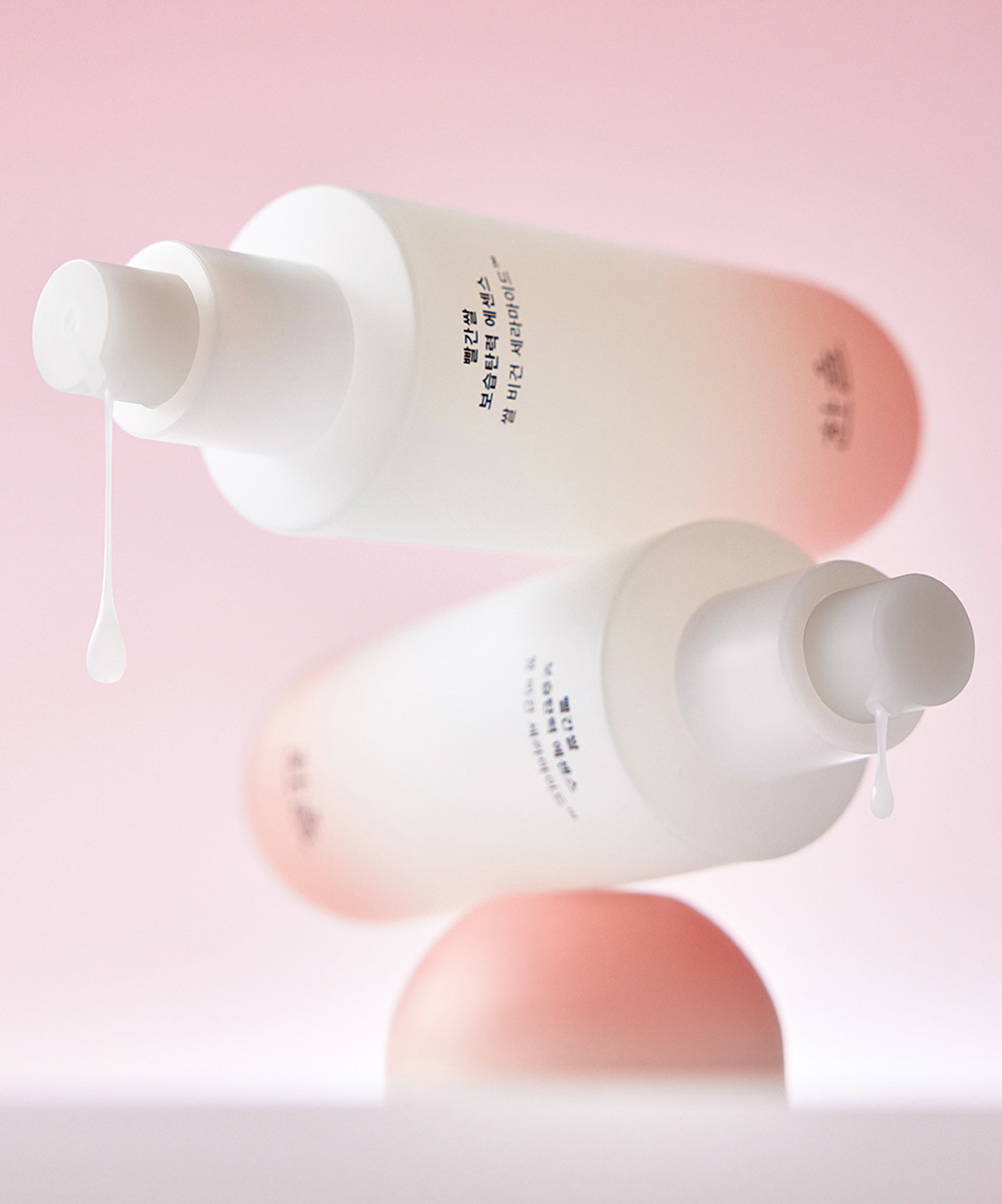 Two bottles of HANYUL Red Rice Moisturizing Elasticity Emulsion with lotion dropping from pumps, set against a pink background.