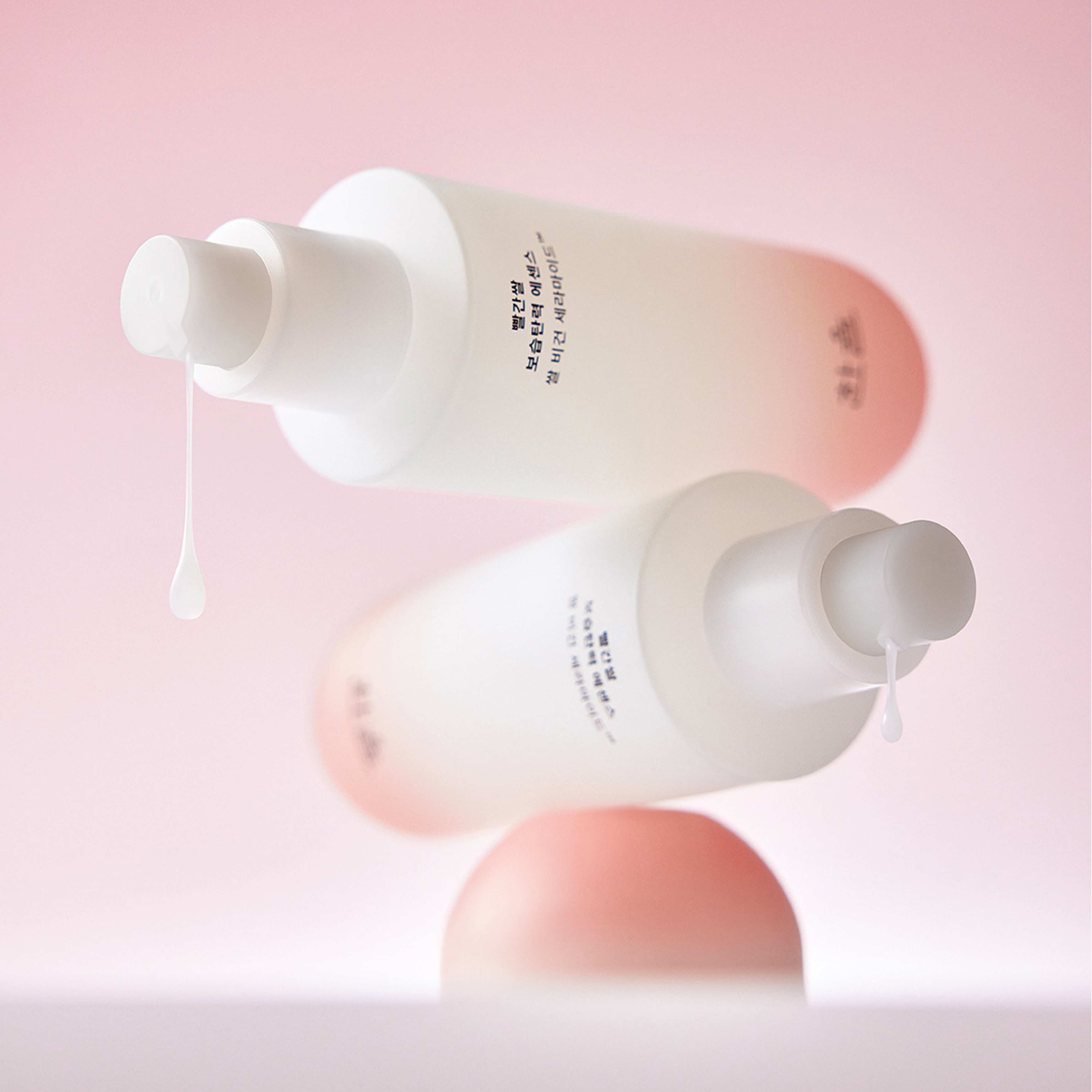 Two bottles of HANYUL Red Rice Moisturizing Elasticity Emulsion with lotion dropping from pumps, set against a pink background.