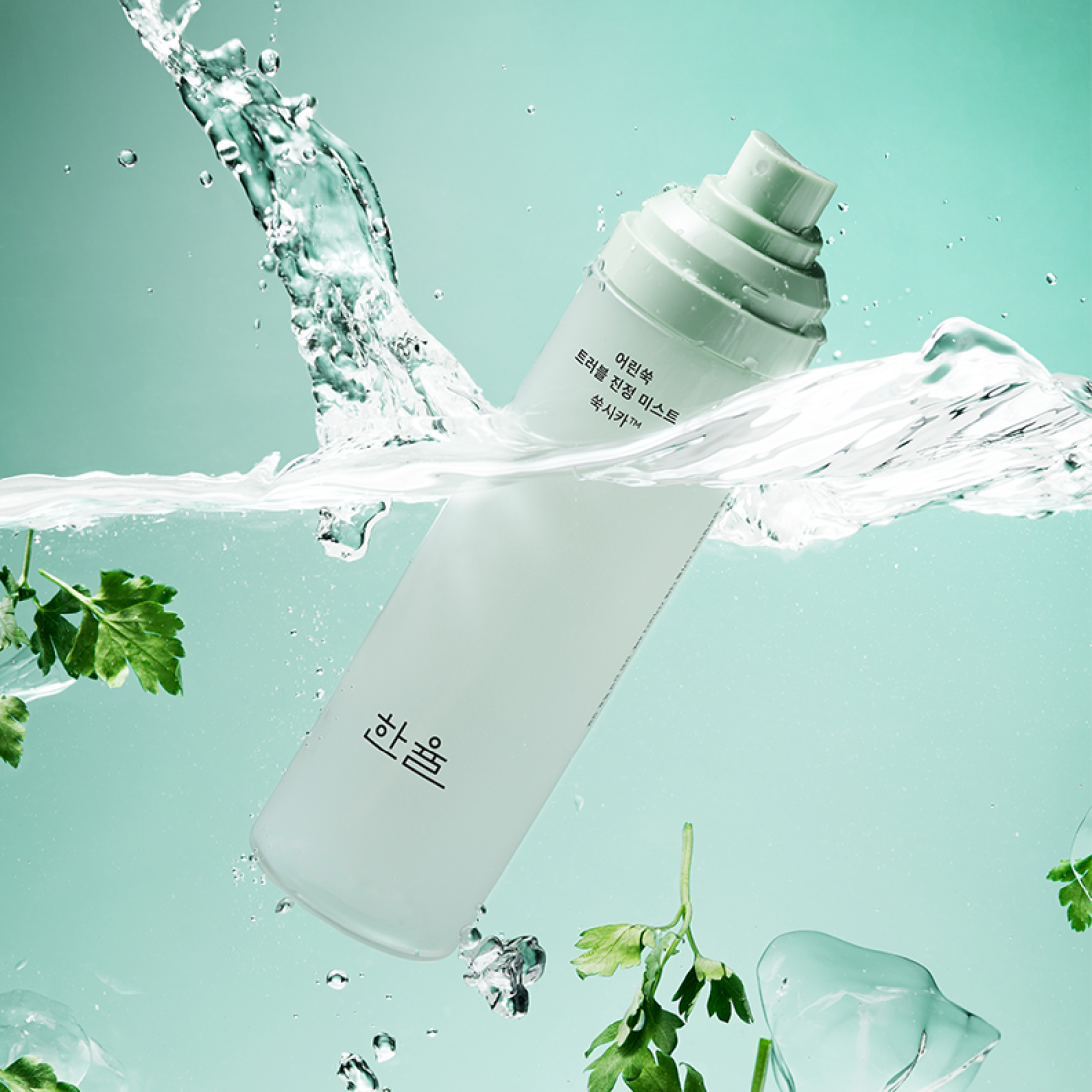 HANYUL Young Artemisia Trouble Mist 120ml bottle surrounded by fresh green herbs and splashing water on a teal background.