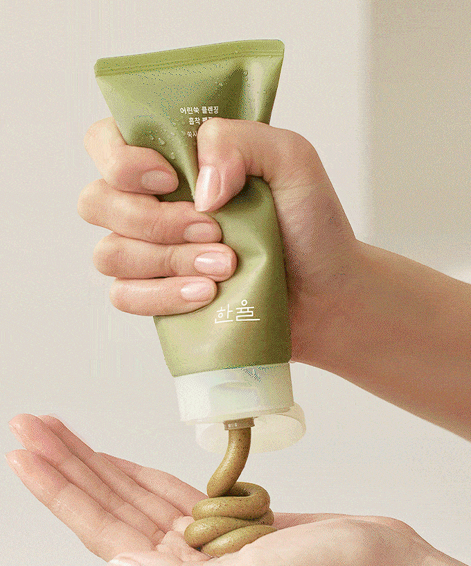 Hands squeezing HANYUL Young Mugwort Cleansing absorption Pack Foam onto palm from a green tube, highlighting product use.